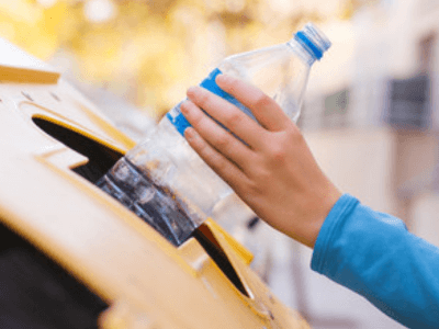 una persona butta una bottiglia di plastica nell'apposito bidone per il riciclaggio